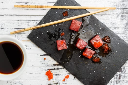 Tuna sashimi dipped in soy sauce with salmon roe, thick salt and dill on slate stone with chopsticks and bowl with soy. Raw fish in traditional Japanese style. Horizontal image.