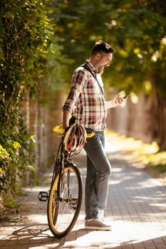 Handsome businessman going to work by bicycle. He is standing next to bike and using smart phone.