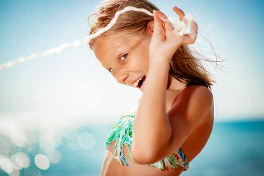 Cute little girl enjoying on the beach. She is poosing and looking at camera with smile on her face.