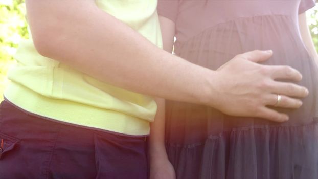 Hands stroking pregnant belly. Husband's hands stroking belly of his pregnant wife. Soft sunset sun illuminates the scene. slowmotion