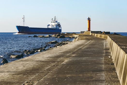 Blue cargo ship sailing against the breakwater dam
