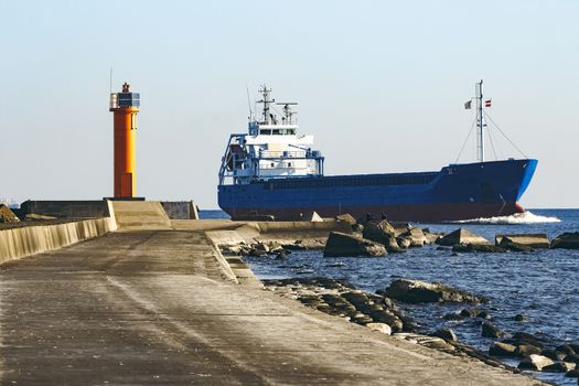 Blue cargo ship sailing against the breakwater dam