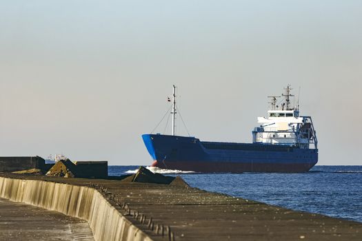 Blue cargo ship sailing against the breakwater dam
