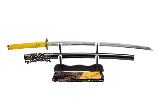 Japanese sword with yellow leather cord wrapped on handle and scabbard with ray skin on stand  white background, black silk bag at front.