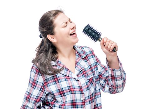 Emotional girl in pajamas singing in hairbrush on white background