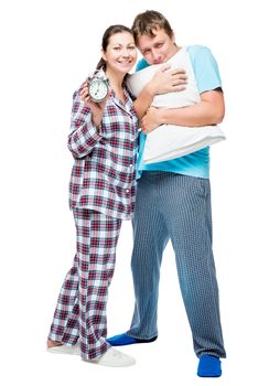 Young couple in pajamas with pillow and alarm clock on white background posing