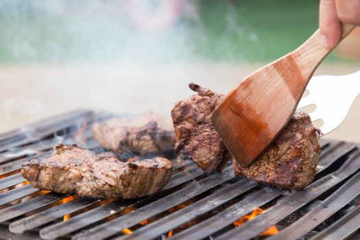 Chef grilling a beef steak on open flame BBQ.