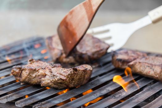 Chef grilling a beef steak on open flame BBQ.