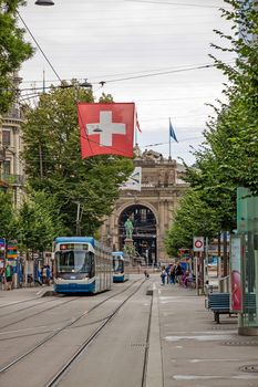 Zurich, Switzerland - June 10, 2017: Shopping promenade called Bahnhofstrasse, inner city of Zurich. Tram / train with swiss flag in front.