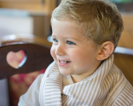 Smile baby boy (18 month) sitting in chair at restaurant, natural light.