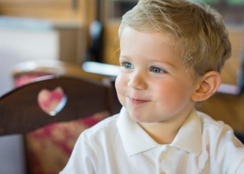 Happy baby boy (18 month) sitting in chair at restaurant, natural light.