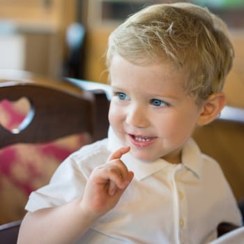 Happy kid boy (18 month) sitting in chair at restaurant, natural light.