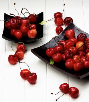 Arrangement of Fresh Ripe Sweet Maraschino Cherries in Two Black Wooden Plates closeup on Plank White background