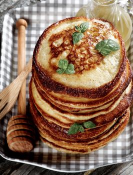 Stack of Homemade Pancakes with Mint Leafs, Honey, Wooden Fork and Honey Dipper closeup in Checkered Tray
