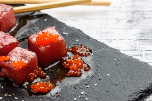 Tuna sashimi dipped in soy sauce with salmon roe, thick salt and dill on slate stone with chopsticks. Raw fish in traditional Japanese style. Horizontal image.