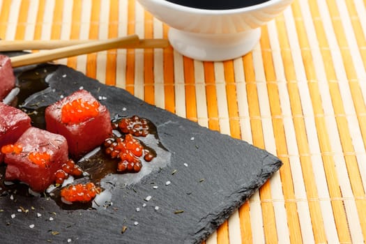 Tuna sashimi dipped in soy sauce with salmon roe, thick salt and dill on slate stone with chopsticks and bowl with soy. Raw fish in traditional Japanese style. Horizontal image.