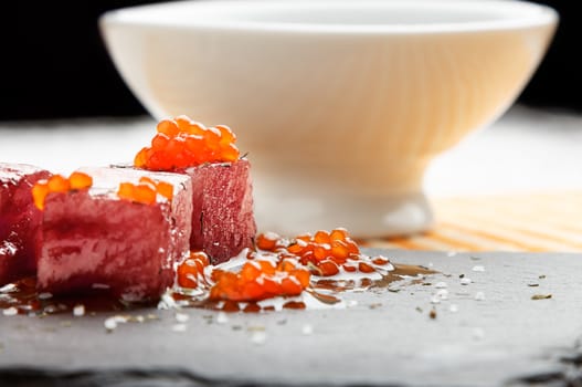 Tuna sashimi dipped in soy sauce with salmon roe, thick salt and dill on slate stone with bowl with soy. Raw fish in traditional Japanese style. Horizontal image.