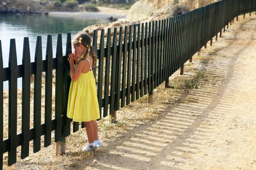 Little girl looks at the sea through a fence
