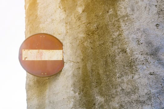 Rusty No entry sign on a ruined wall. Sun backlight