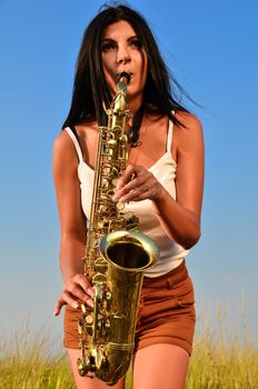 Beautiful girl plays the saxophone in the summer on the nature