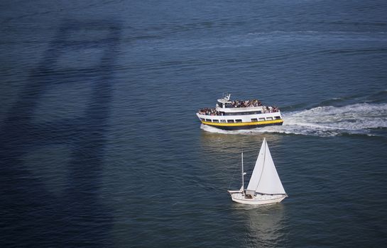 A ferry and sail boat cruising under the Golden Gate Bridge in San Francisco Bay.