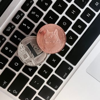 Cryptocurrency physical silver Litecoin coin and brass Dogecoin money on the black computer keyboard.