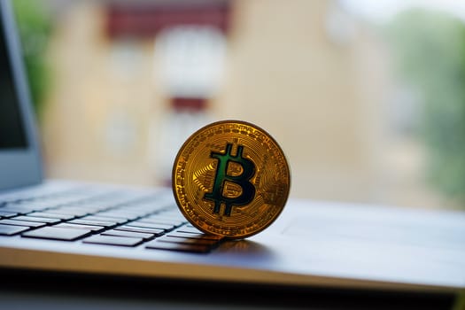 Cryptocurrency physical gold bitcoin coin on the computer keyboard near window.
