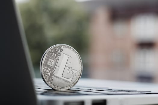 Cryptocurrency physical silver Litecoin coin on the black computer keyboard near the window.