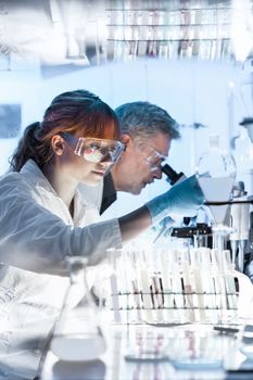 Health care researchers working in life science laboratory. Young female research scientist and senior male supervisor preparing and analyzing microscope slides in research lab.