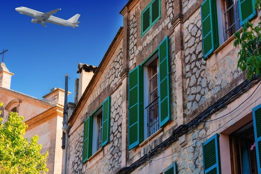 Buildings in the village of Valldemossa on the island of Majorca in Spain. In the background in the sky a passenger airplane.