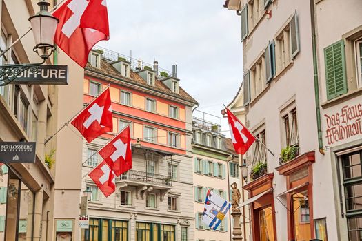 Zurich, Switzerland - June 10, 2017: Old street in downtown Zurich with old colorful buildings with national flags.