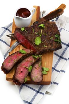 Delicious Roast Beef Medium Rare Sliced on Wooden Cutting Board with Tomato Sauce, Fork and Table Knife closeup on Checkered Napkin