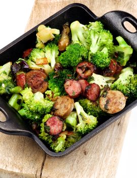 Homemade Stew with Broccoli and Grilled Sausages in Black Iron Cast on Wooden Board isolated on White background