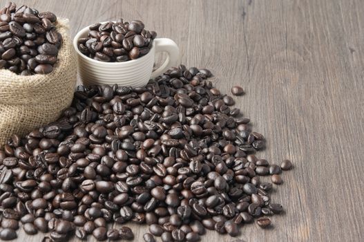 Stack of coffee bean in white cup and brown sack on wooden background.