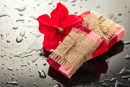 Handmade soap red with a flower petunia on black background and drops of water