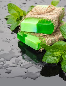 Handmade soap green with mint leaves on a black background and drops of water
