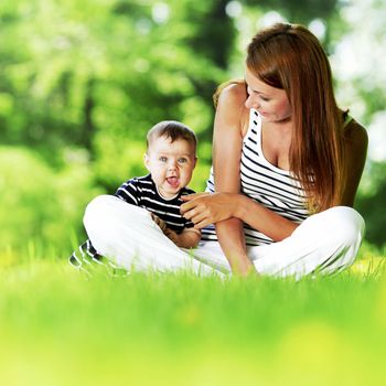 Mother and daughter sitting on grass in spring park