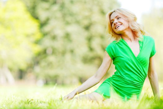 Beautiful young blond woman sitting on grass in park