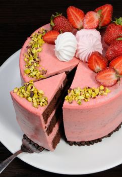 A cut piece of chocolate strawberry mousse cake decorated with berries, meringue and pistachios