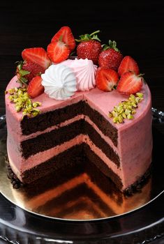 Chocolate strawberry cake decorated with berries, meringue and pistachios in a cut