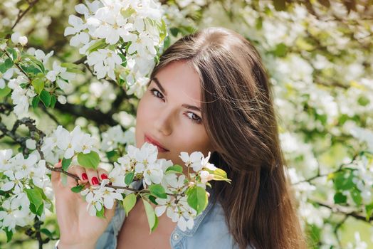 Beautiful young brunette woman standing near blooming apple tree