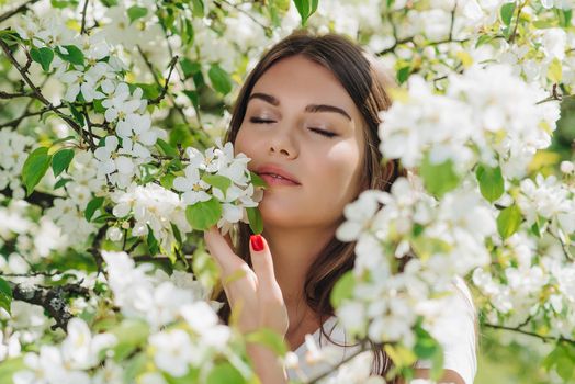 Beautiful young brunette woman standing near blooming apple tree