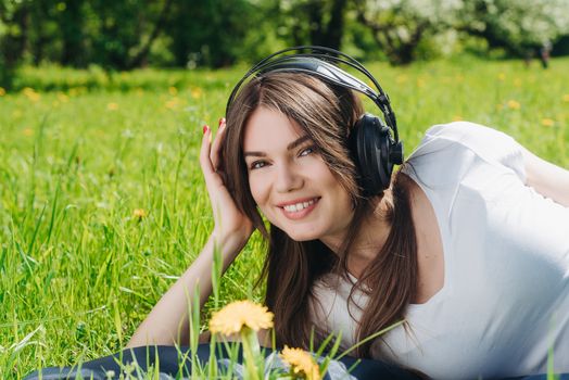 Young brunette woman with headphones listening to the music outdoors on sunny summer day