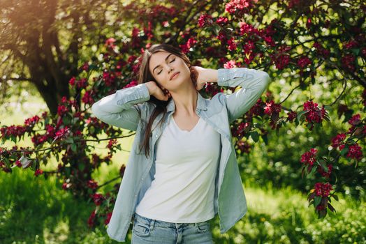 Beautiful young brunette woman standing near blooming tree with red flowers