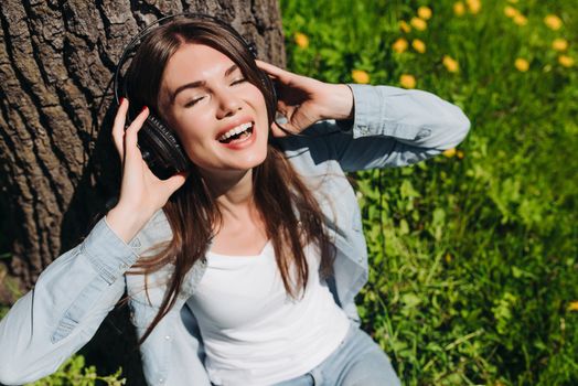 Young brunette woman with headphones listening to the music in park on sunny summer day