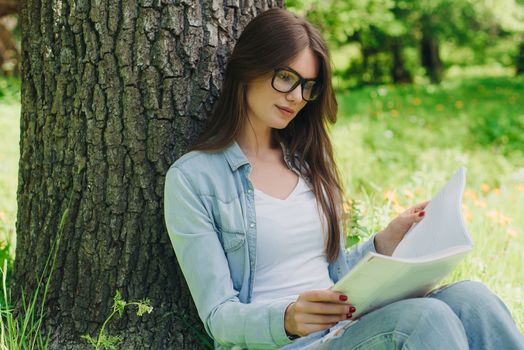 Beautiful young brunette sitting on a fallen autumn leaves in a park, reading a book