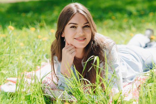 Beautiful young woman laying on grass with dandelion flowers in park