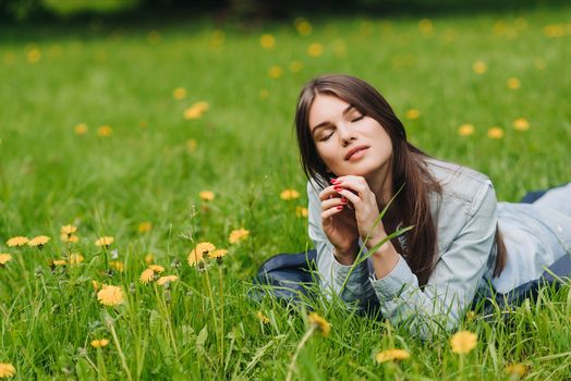 Beautiful young woman laying on grass with dandelion flowers in park