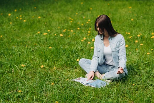 Beautiful young woman reading a book on grass with dandelion flowers in park