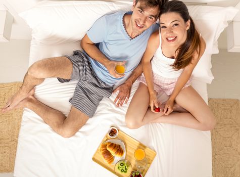 Young couple eating the breakfast on the bed